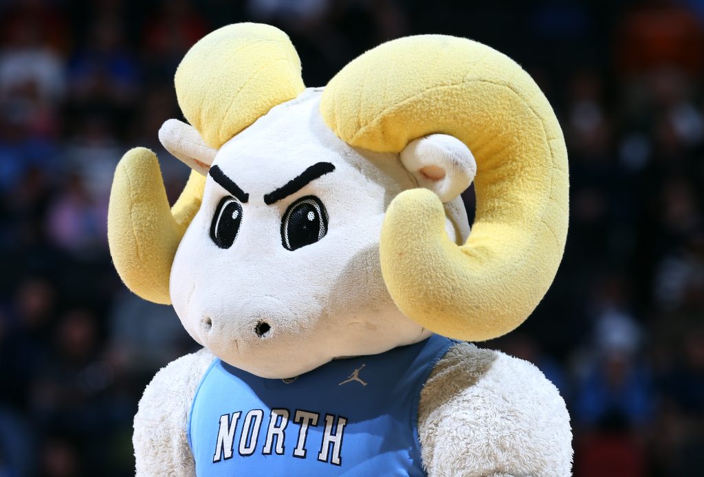 The North Carolina Tar Heels mascot, Rameses, is a plush ram with large yellow horns, intimidating eyebrows and large eyes. He is wearing a Carolina Blue Tarheels Basketball jersey.